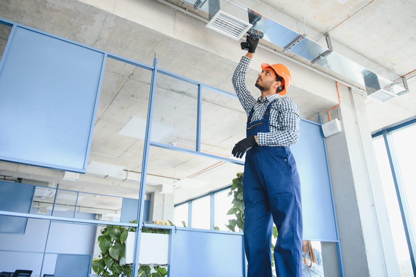 A technician servicing overhead ventilation in a building